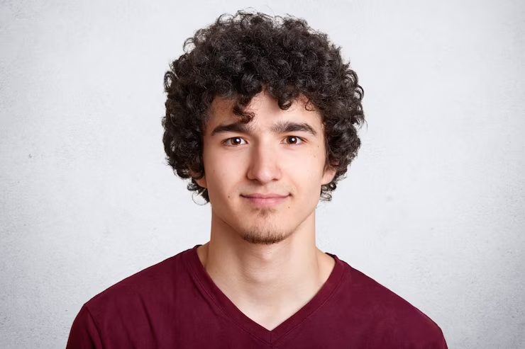 A young man with curly hair in a maroon shirt.
