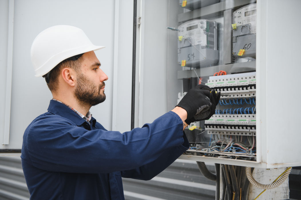 An electrical engineer in a safety helmet inspecting a circuit breaker panel, representing professional Engineering Consultancy in Abu Dhabi.